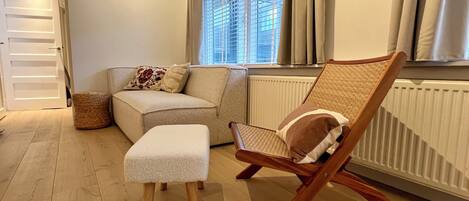 Una sala de estar acogedora con un sofá, una silla de madera y un pequeño reposapiés.
