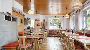 Ein Restaurant mit Holztischen, großen Fenstern und hängenden Pendelleuchten.