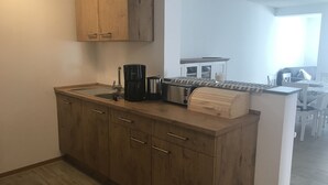 Cuina compacta amb armaris de fusta, un cafetera, un torradora i una caixa per al pa.