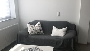 Un saló amb un sofà gris, dos coixins estampats, una taula de centre i una obra d'art amb temàtica de platja a la paret.