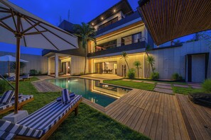 A modern house with a swimming pool, wooden deck, and lounge chairs. - Villa Sunset Berawa (Canggu)