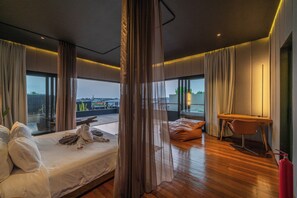A modern hotel room with a large bed, a desk, and a view of the cityscape. - Villa Sunset Berawa (Canggu)