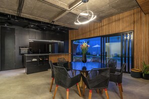 A modern kitchen with a dining area, featuring a round table with chairs, a vase with flowers, and a view through large glass doors. - Villa Sunset Berawa (Canggu)
