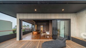 A modern interior with a wooden floor, a bean bag chair, and a glass door leading to a balcony. - Villa Sunset Berawa (Canggu)