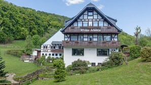 Un hôtel de style chalet traditionnel, doté d’un balcon imposant, entouré d’une végétation luxuriante et offrant une vue sur un ciel dégagé.