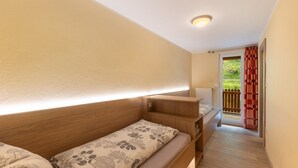 Une chambre avec deux lits, une tête de lit en bois, une table de chevet et une fenêtre donnant sur un paysage verdoyant.
