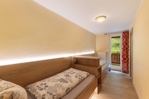 Une chambre avec deux lits, une tête de lit en bois, une table de chevet et une fenêtre donnant sur un paysage verdoyant.