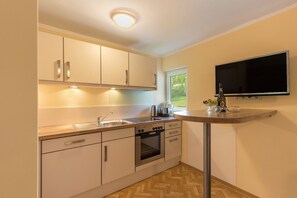 A modern kitchen with white cabinets, a stainless steel oven, a sink, and a flat-screen TV mounted on the wall.