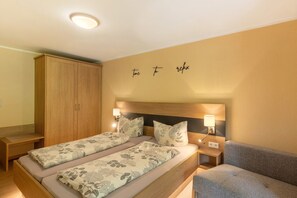 A double bed with floral bedding, a wooden wardrobe, bedside lamps, and a couch.