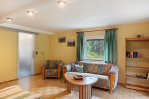 Een woonkamer met een bank, fauteuil, houten salontafel, boekenkast en een schuifdeur.
