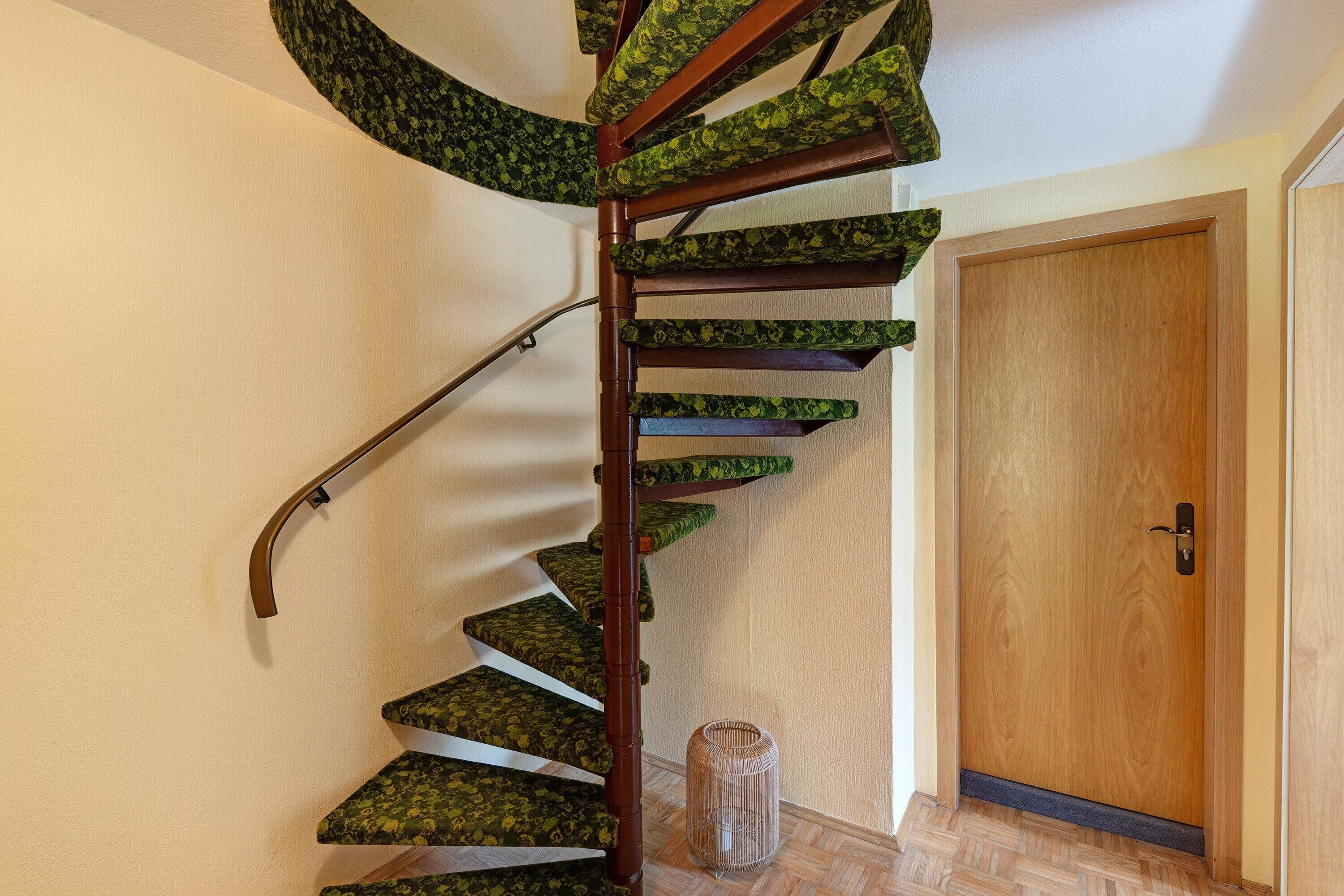 A spiral staircase with a wooden handrail and green patterned steps.