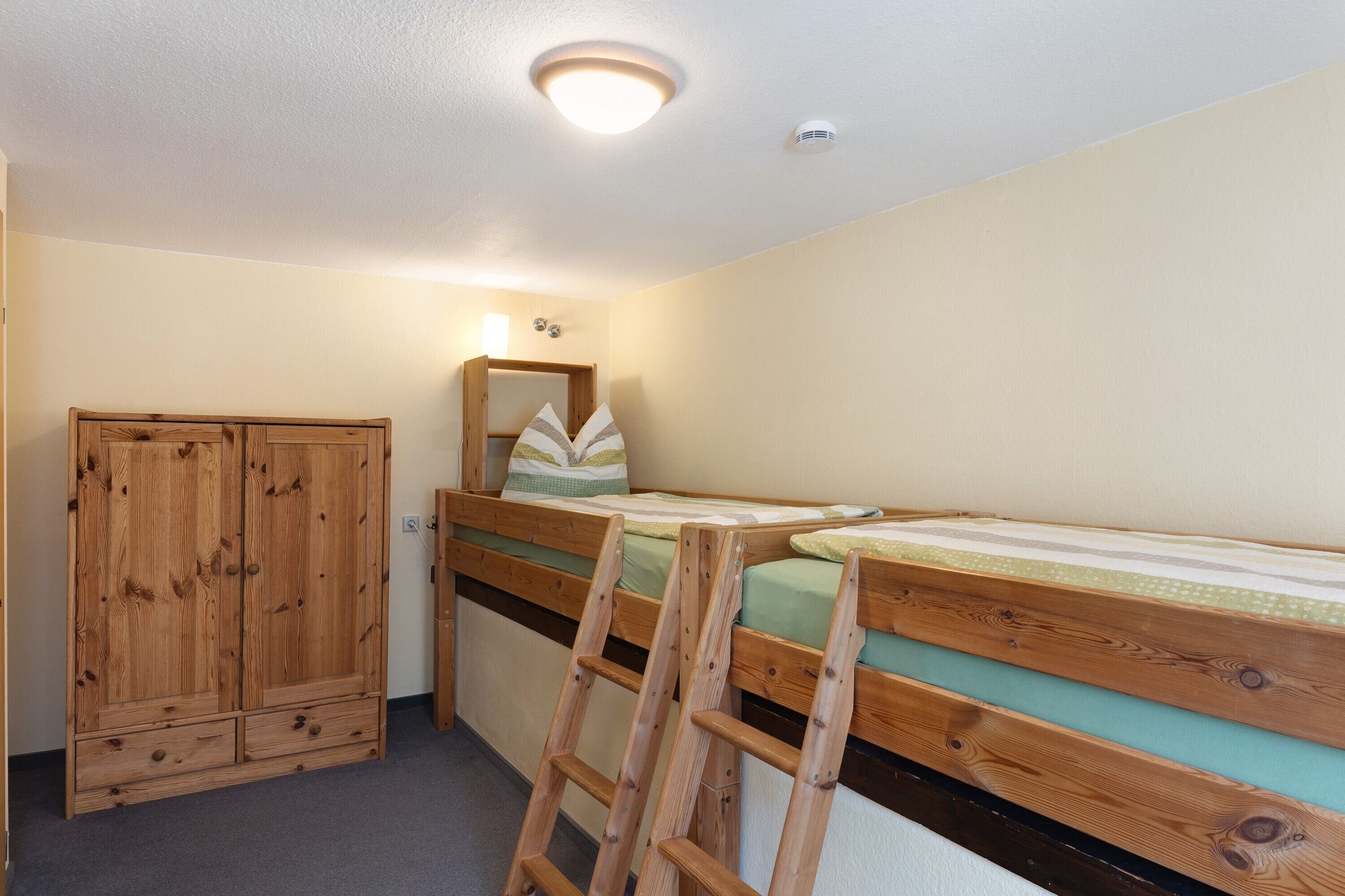 A bedroom with a wooden wardrobe, a bed with a green mattress, and a wooden ladder.