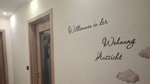 A hallway with a welcome sign on the wall, wooden doors, and a cloud decoration.