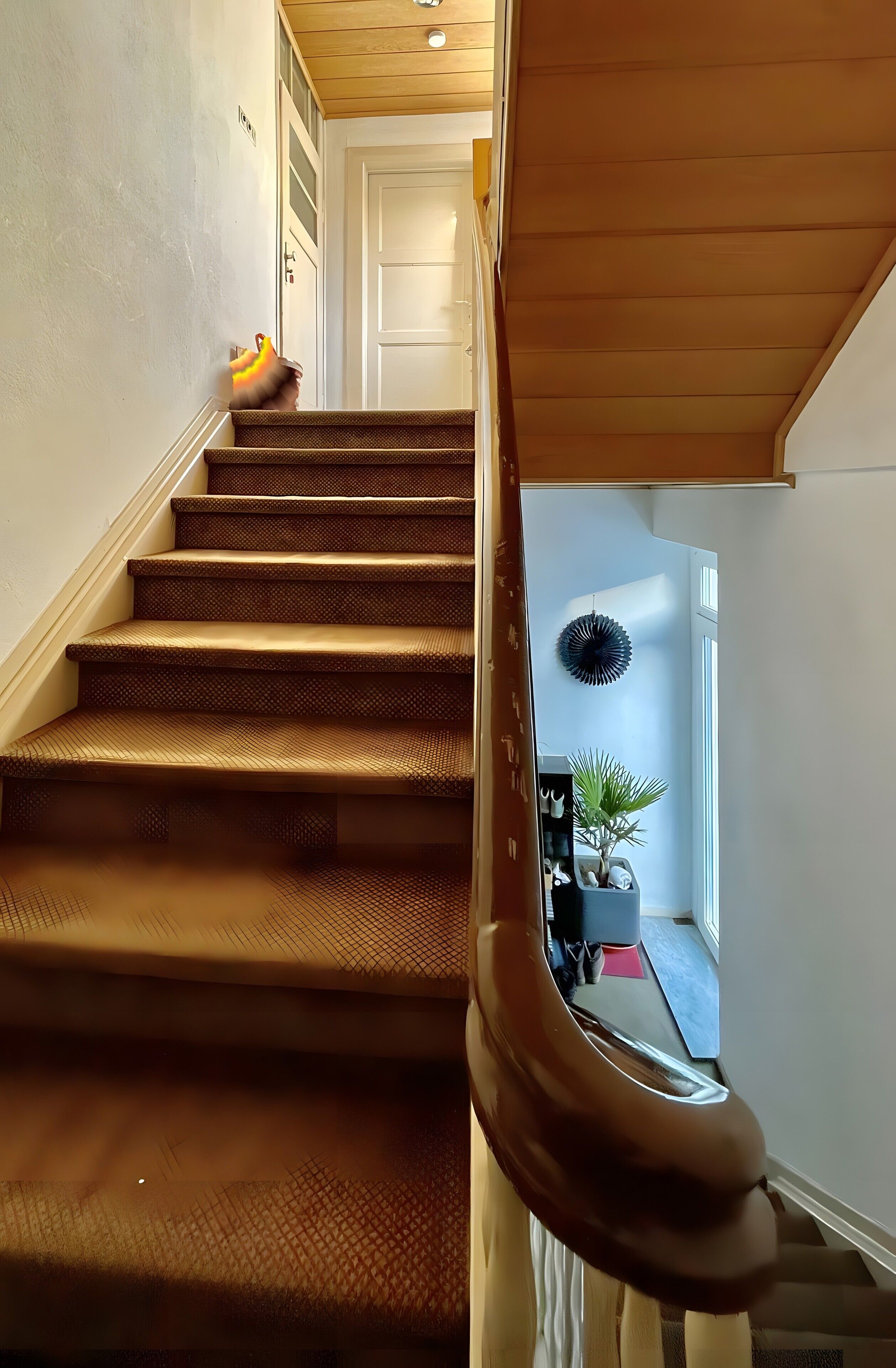 Eine Treppe mit hölzernem Geländer und Blick in einen Raum mit Pflanze und Tür.