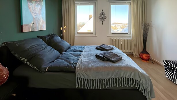 Une chambre à coucher avec un lit, deux fenêtres, un tableau, une décoration murale et une lampe sur pied.