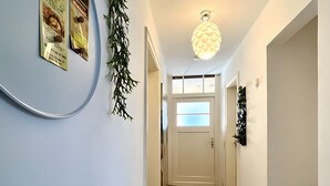 Un couloir doté d’un plancher en bois, d’une porte blanche avec des panneaux en verre dépoli et d’un luminaire au plafond.