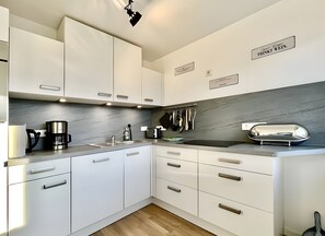 A modern kitchen with white cabinets, a coffee maker, a toaster, and kitchen utensils hanging on the wall.