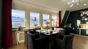 Un salon moderne comprenant un coin repas, de grandes fenêtres, un radiateur, un téléviseur et une bibliothèque.