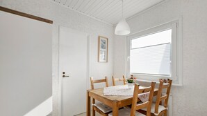 Een eetgedeelte met een houten tafel en stoelen, een hanglamp, een raam met jaloezieën en een deur met behangpapier met een patroon.