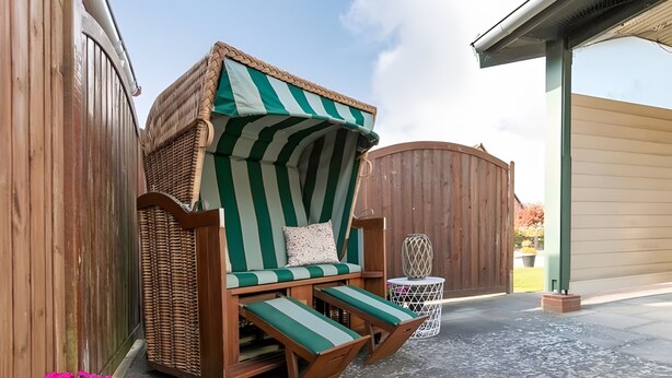 Een rieten lounge stoel met een gestreept kussen, een klein rond tafeltje en een witte mand.