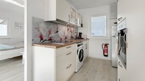 Een compacte keuken met een wasmachine, een brandblusser en een bed in de aangrenzende kamer.