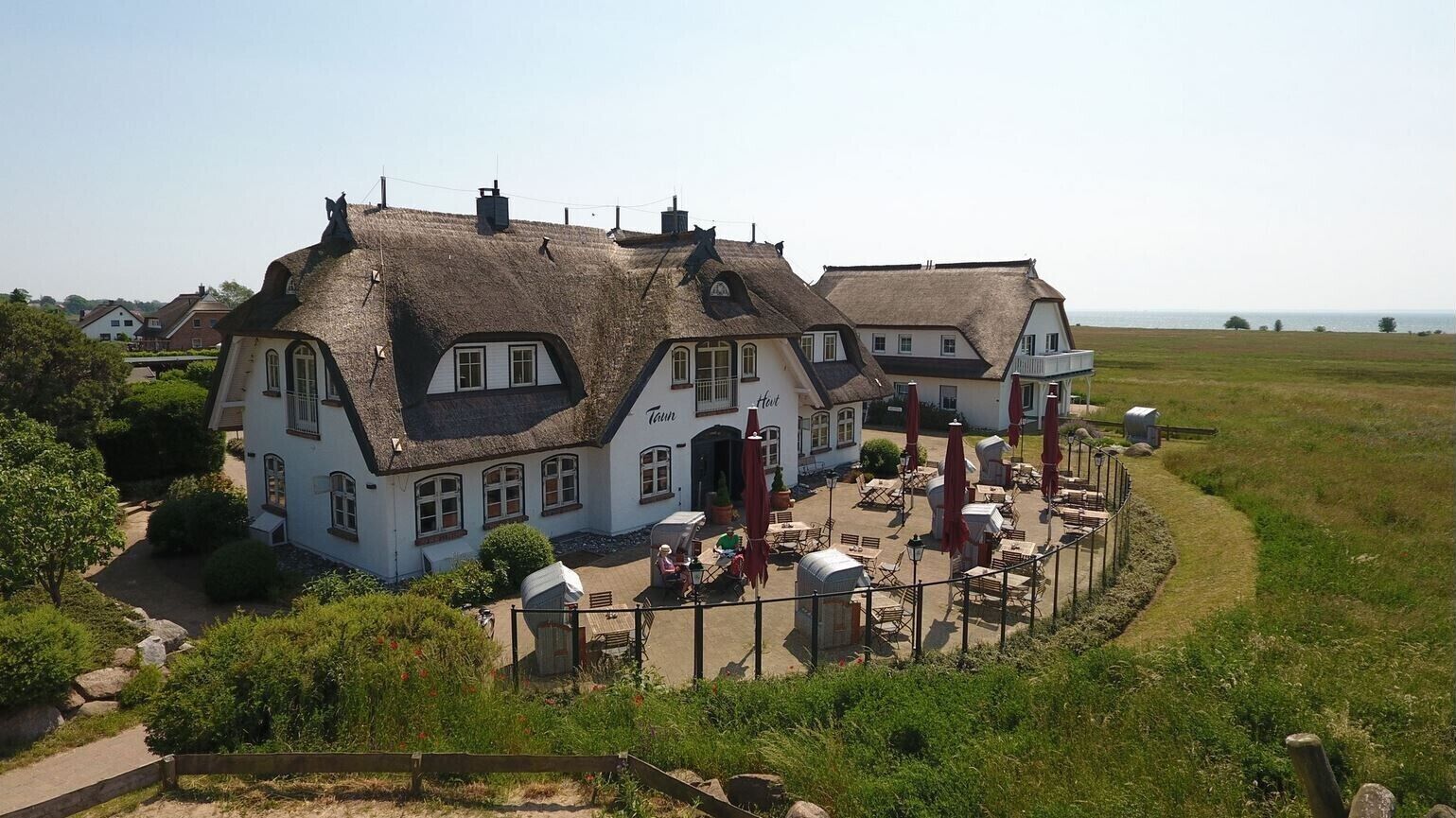 A traditional building with a thatched roof, a patio area with outdoor seating, and a view of the sea.