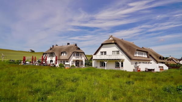 Two white houses with thatched roofs, a grassy field, and red umbrellas.