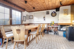 A wooden dining area with a table and chairs, a dartboard, a clock, and a whiteboard on the wall.