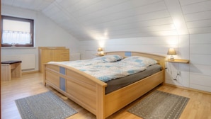 Un dormitorio con una cama de madera, lámparas de noche, una ventana con cortinas, un radiador y un banco.