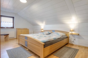 A bedroom with a wooden bed, bedside lamps, a window with curtains, a radiator, and a bench.