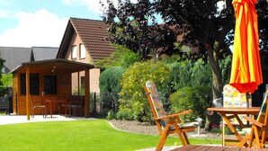 Una casa de madera con un patio, mobiliario exterior y un muro de piedra.