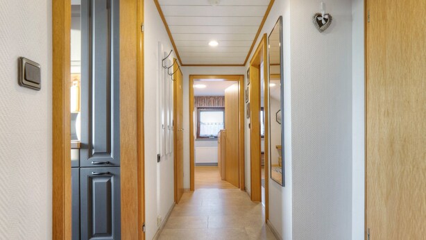 Un pasillo con puertas de madera, una zona de cocina y un ventanal con cortinas.