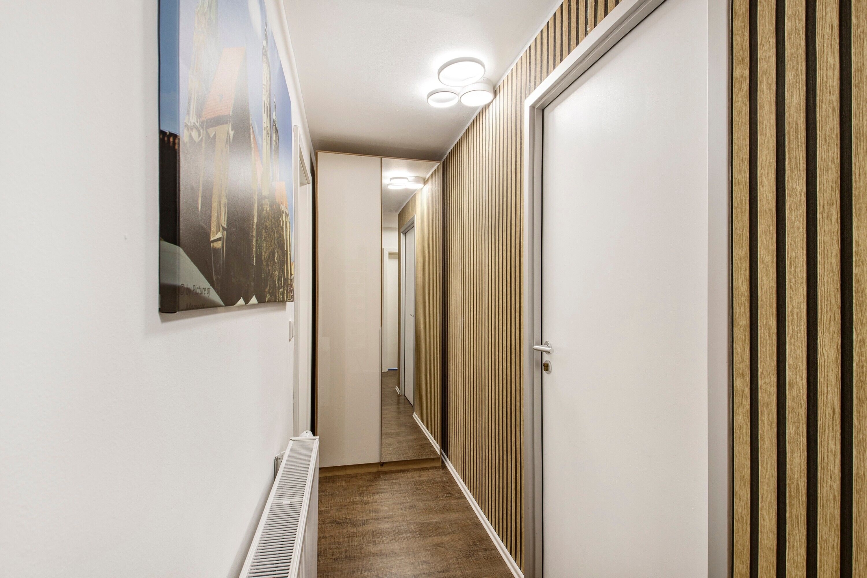 A hallway with a radiator, a wooden door, and a poster on the wall.