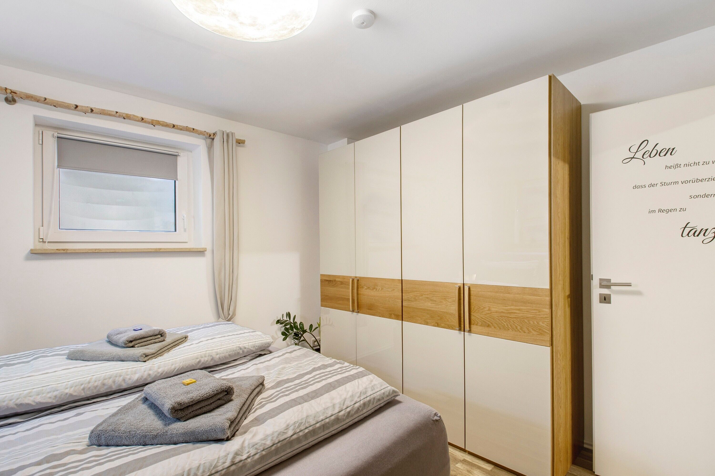 Ein Schlafzimmer mit Bett, Kleiderschrank, einem Fenster mit Vorhängen und einer Wand mit Schrift.