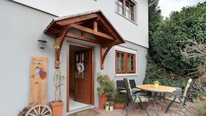 Een huis met een houten veranda, een deur, een raam en een tafel met stoelen.