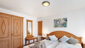 Een slaapkamer met een houten bed, een nachtkastje, een kast en een schilderij aan de muur.