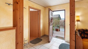Een gang met een houten deur, een kleedje en een bank met een gekleurd kussen.
