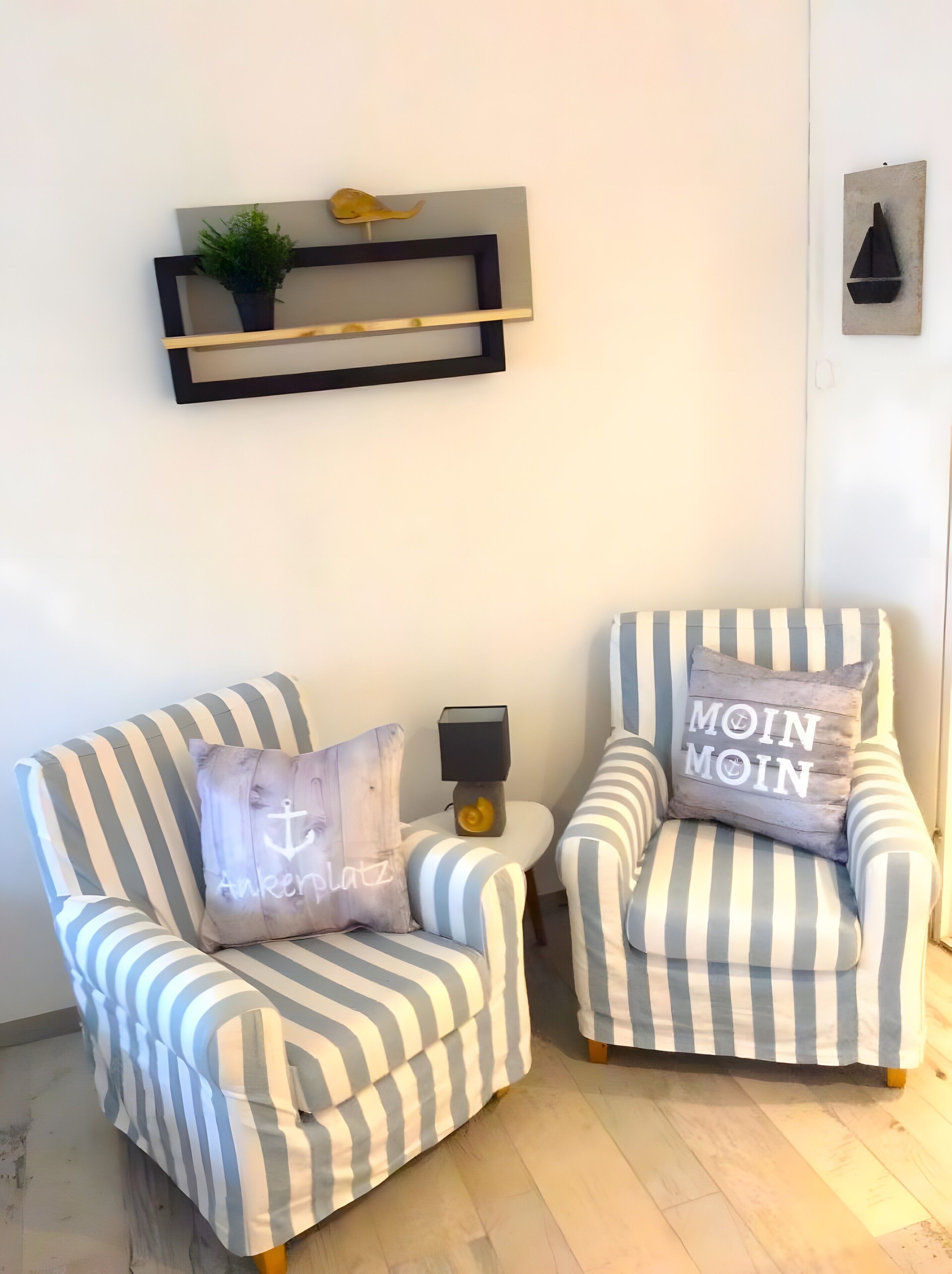 Two striped armchairs with cushions, a small side table with a lamp, and a wall-mounted shelf with a plant and decorative items.