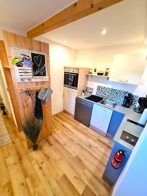 A modern kitchen with wooden flooring, a built-in oven, a dishwasher, and a coffee machine.