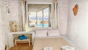Ein Zimmer mit Bett, einem kleinen Tisch mit Lampe, einem Fenster mit Vorhängen und Meerblick.