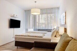 Une chambre moderne avec un lit, une télévision, une fenêtre avec des rideaux, un radiateur et un canapé.