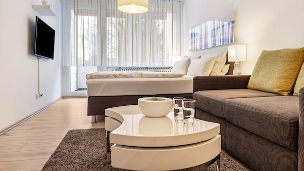 A modern hotel room with a bed, a sofa, a television, a dining table, and a window with curtains. - Vacation apartment '2' with Wi-Fi (Meersburg)