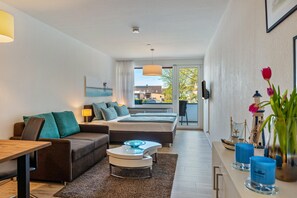 Habitación de hotel moderna con cama, sofá, mesa de centro y vistas al exterior.