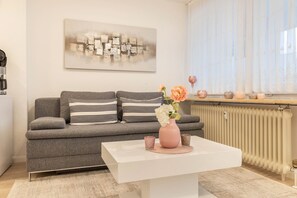 A modern living room with a grey sofa, a white coffee table, and a pink vase with flowers.