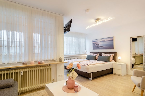 Une chambre à coucher moderne, avec un lit, une table de chevet, une commode et une grande fenêtre avec des rideaux.