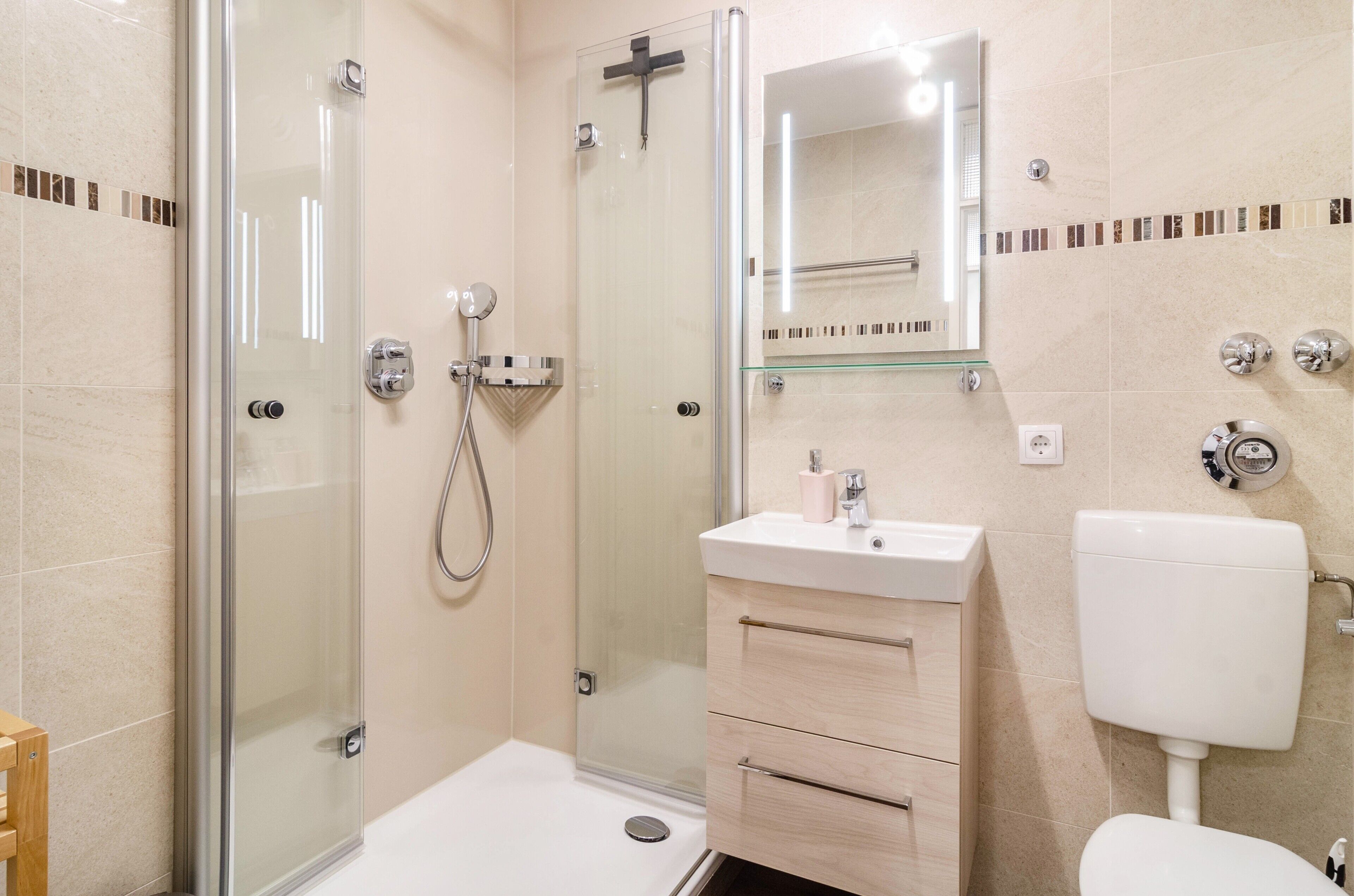 Ein modernes Badezimmer mit Duschkabine aus Glas, einem Waschbecken mit Spiegel darüber und einer Toilette.