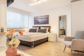 Une chambre à coucher avec un lit, des tables de chevet, une chaise, un miroir et un tableau accroché au mur.