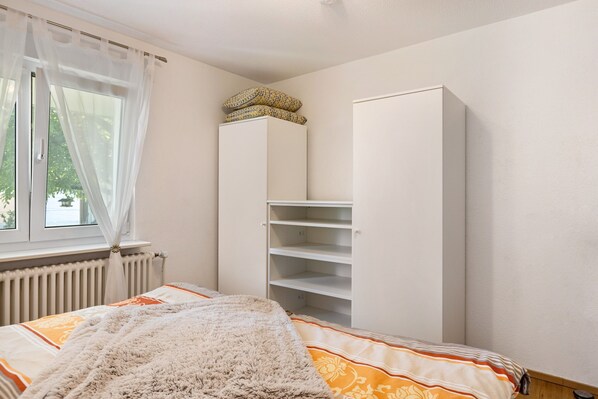 A bedroom with a bed, a wardrobe, a radiator, and a window with sheer curtains.