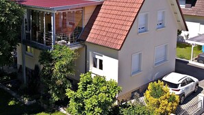 A two-story house with a red-tiled roof, a balcony, and a car parked in the driveway. - Quiet, Modern Apartment with Garden near Lake Steißlingen and Lake Constance (Steißlingen)
