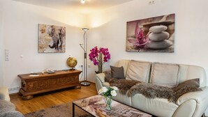 A living room with a sofa, a wooden sideboard, a globe, and a painting of stacked stones. - Quiet, Modern Apartment with Garden near Lake Steißlingen and Lake Constance (Steißlingen)